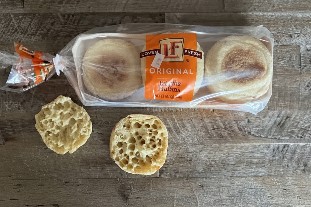L'oven Fresh Original English Muffins lifestyle shot on rustic wood with two fork-split muffins showing classic nooks and crannies texture